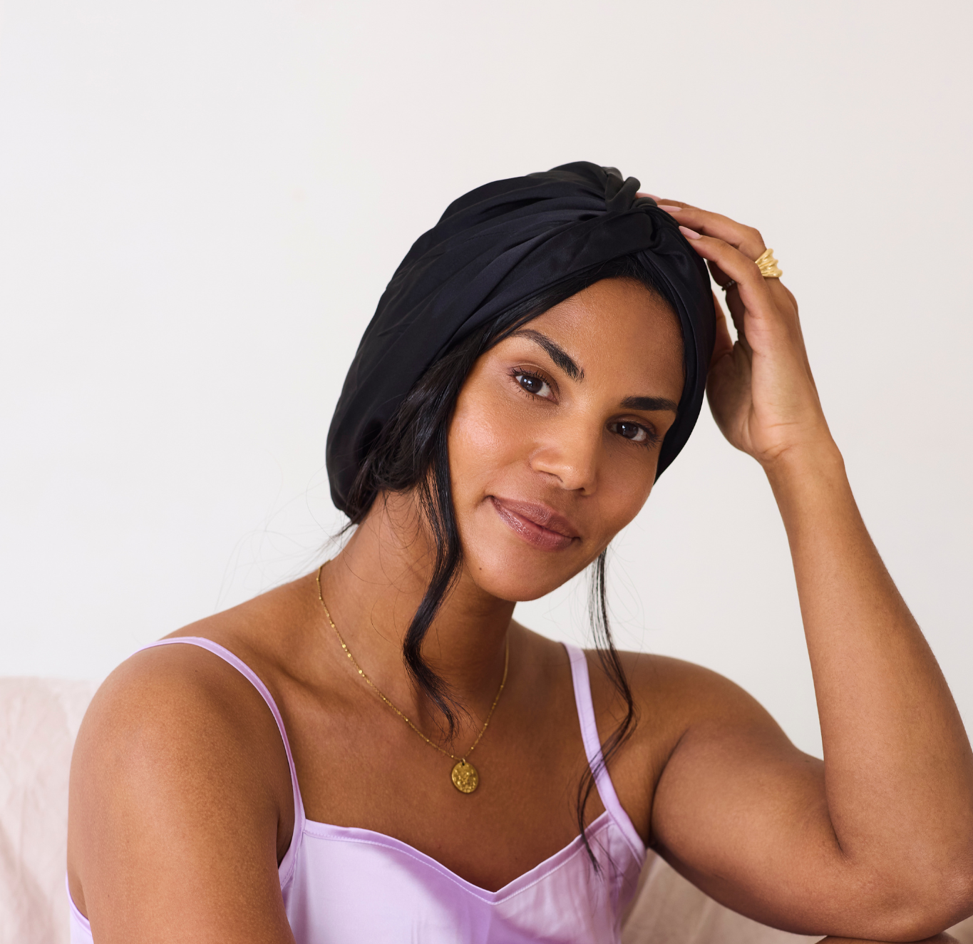 Woman in a purple satin pyjamas and black silk bonnet sitting on a white background