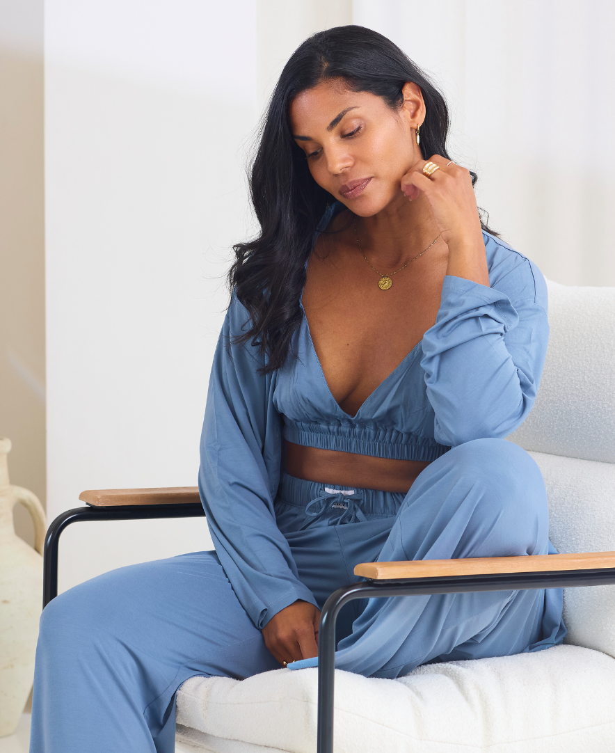 Woman in a blue pyjamas sitting on a white chair in a minimalistic room.